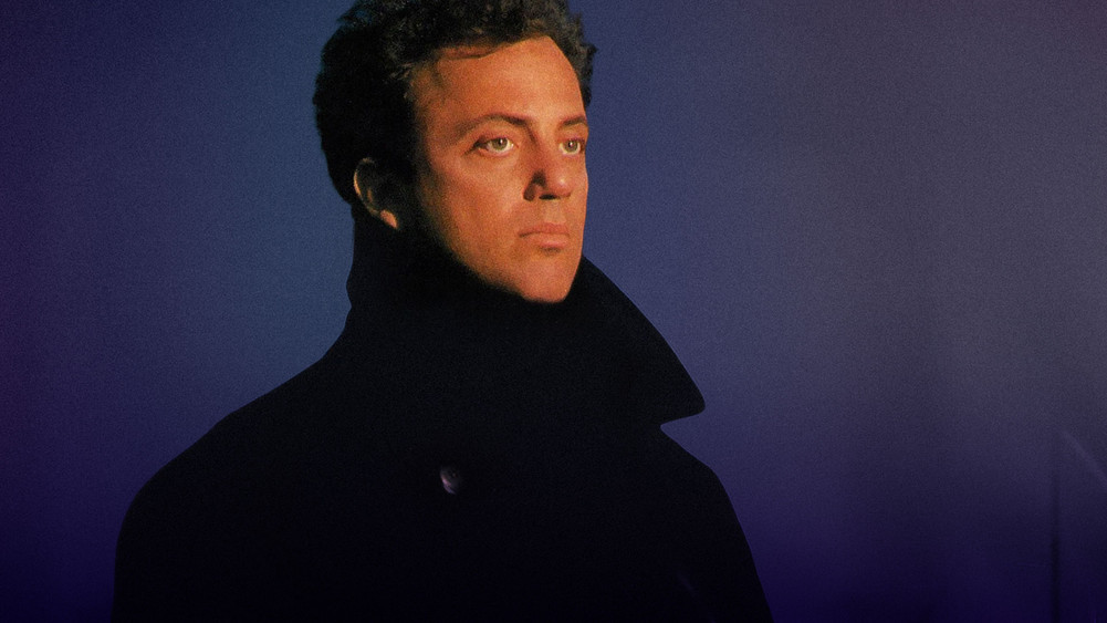 Billy Joel sitzt vor einem dunkelblauen Hintergrund