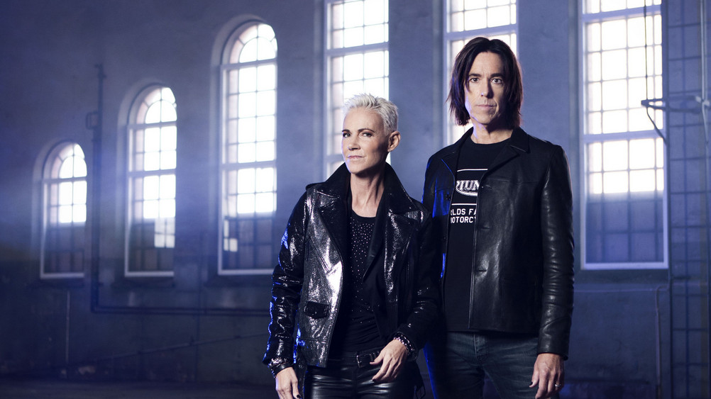 Roxette stehen zusammen vor einer Reihe großer Fenster